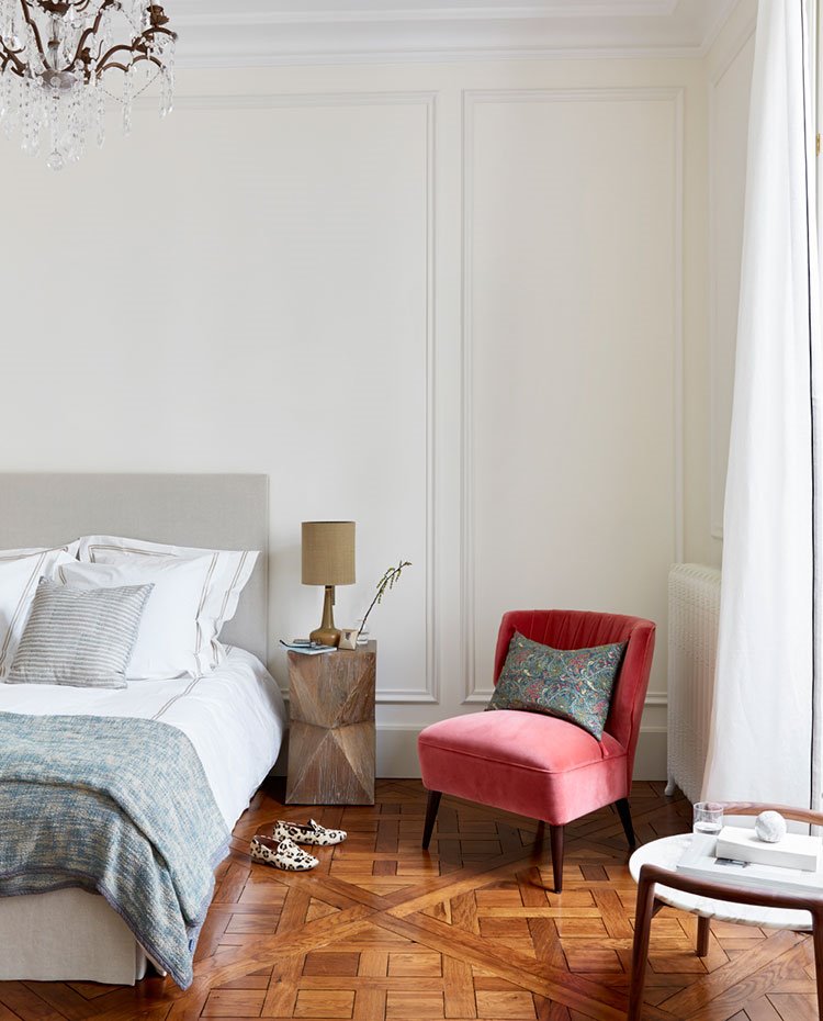 Dormitorio con cama y colcha en azul grisáceo, butaca en rojo, mesilla con lámpara a juego