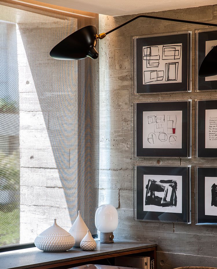 Objetos decorativos en blanco, luminaria negra con brazo, cuadros simétircos en pared de hormigón
