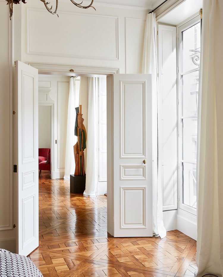 Puertas con molduras en blanco, suelo de madera, escultura y amplios ventanales