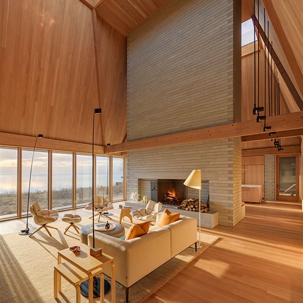 Salón de gran altura con cerramientos acristalados hacia lago, mobiliario de tonos crudos y en madera