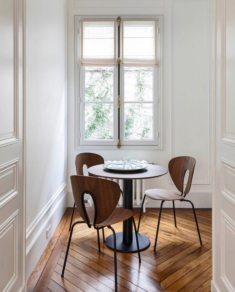 Sillas de madera, mesa redonda, suelo de madera y puertas con modulras
