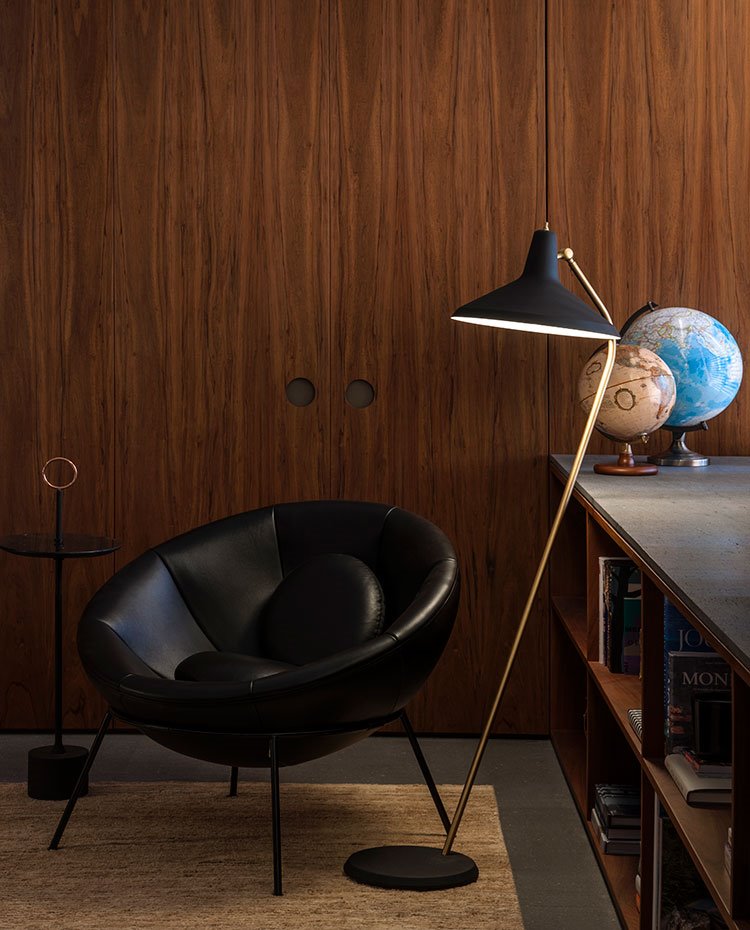Zona de lectura con butaca de piel negro, lujminaria de pie y globos terráqueos sobre módulo bajo