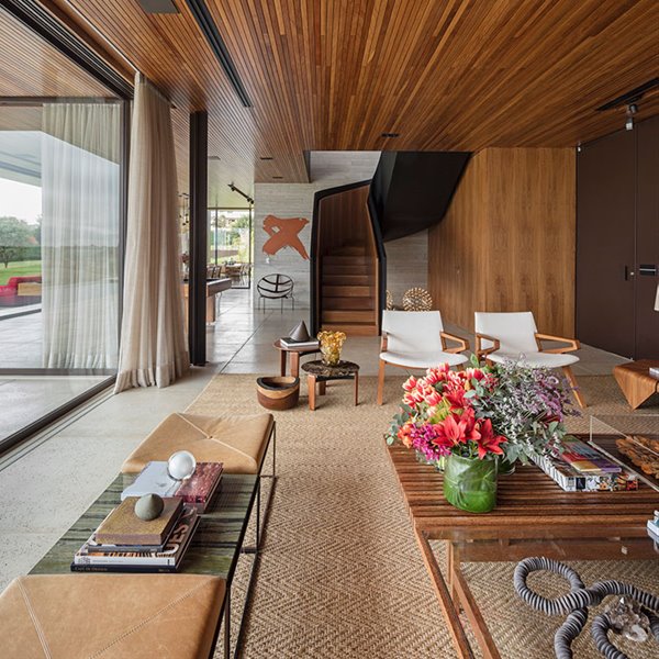 Salón con mesa de centro en madera y cristal, bancada de cuero y estrucutra metalizada frente a cerramiento corredero de cristal, cortinas en grudo y techo de madera