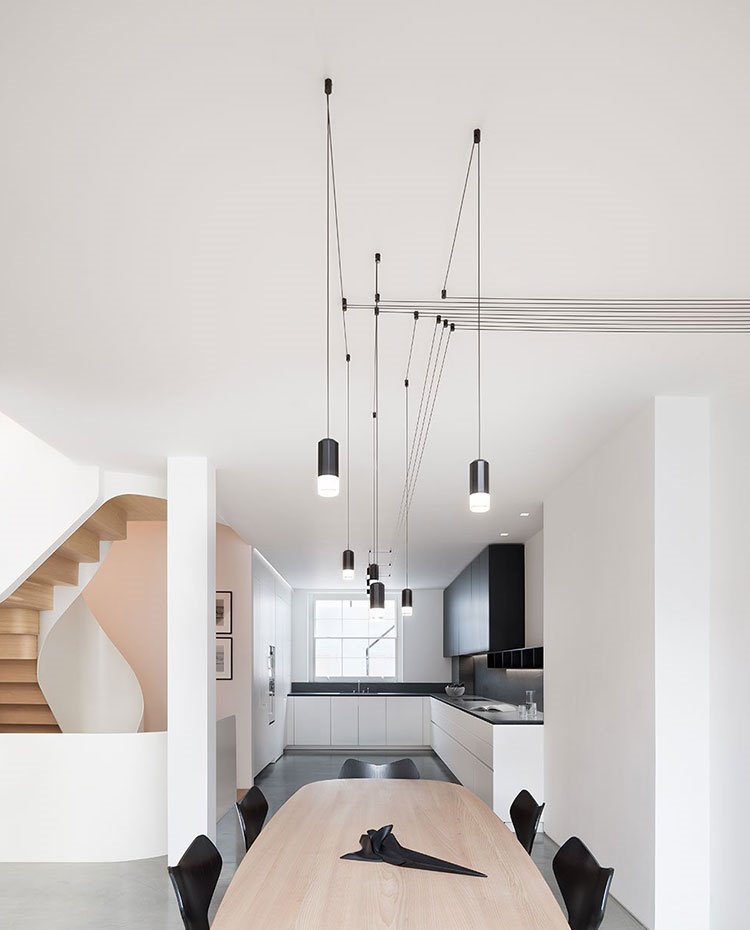 Cocina abierta en forma de L, planta diáfana con mesa de comedor en madera, sillas en negro, suelo de hormigón