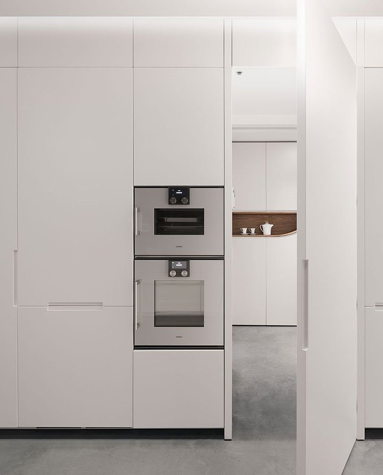 Cocina con mobiliario totalmente en blanco. puerta con tirador integrado, suelo de hormigón