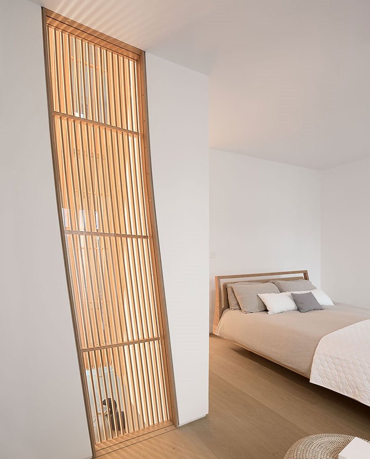 Dormitorio con detalle en pared en madera, pouf de fibra natural, suelo de madera, cama con ropa de hogar en tonos crudos