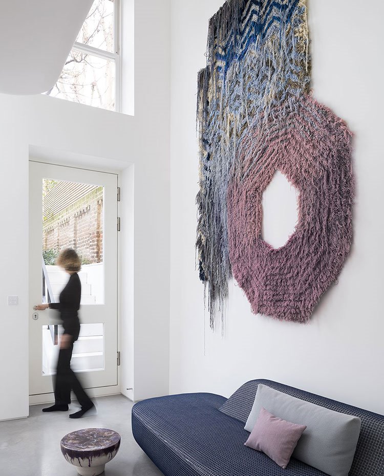 Puerta de acceso a la vivienda con sofá azul junto a mesita y tapiz a pared