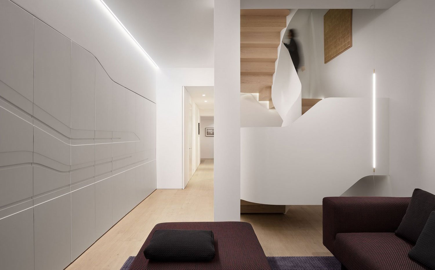 Zona de estar en nivel inferior, armarios integrados en estructura de pared, sofás en burdeos, suelo de madera
