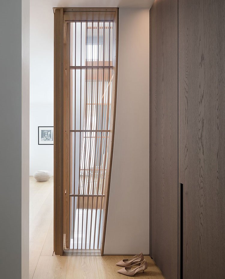 Zona vestidor con armarios hechos a medida con tiradores integrados en madera oscura, suelo de madera, hueco escalera con estructura de madera