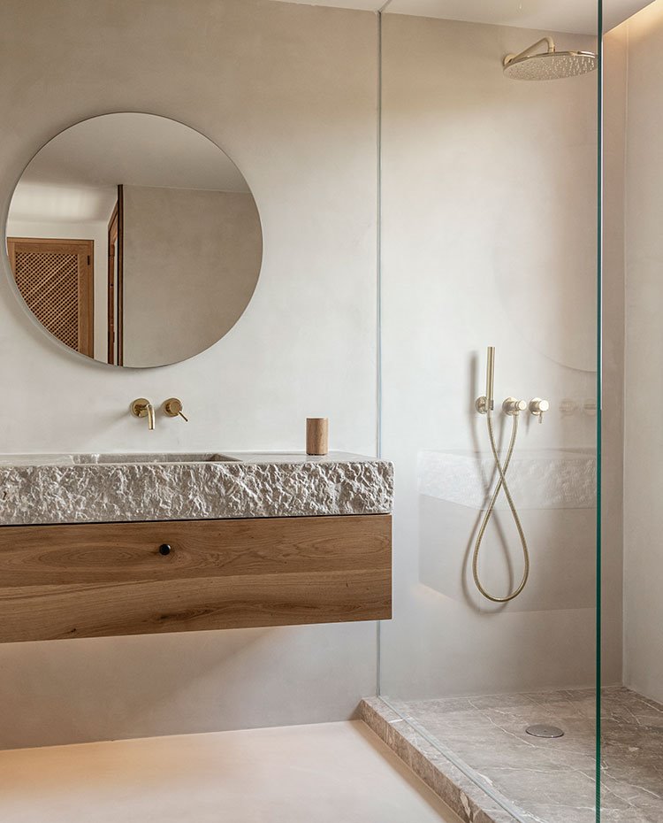 Cuarto de baño con plato de ducha de piedra, a juego con encimera, mueble de madera suspendido, espejo circular