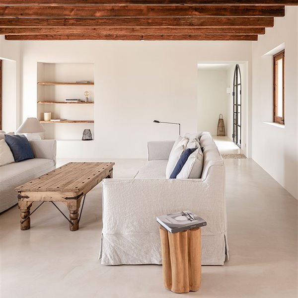 Salón con sofás enfrentados en tonos gris claro, mesa de centro de madera y vigas en techo 
