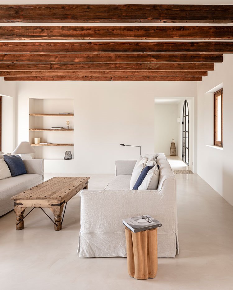 Salón con sofás enfrentados en tonos gris claro, mesa de centro de madera y vigas en techo 