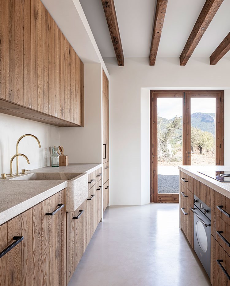 Zona de trabajo de cocina, con mobiliario en madera natura alistonada, tirados en negro, encimera en tonos crema