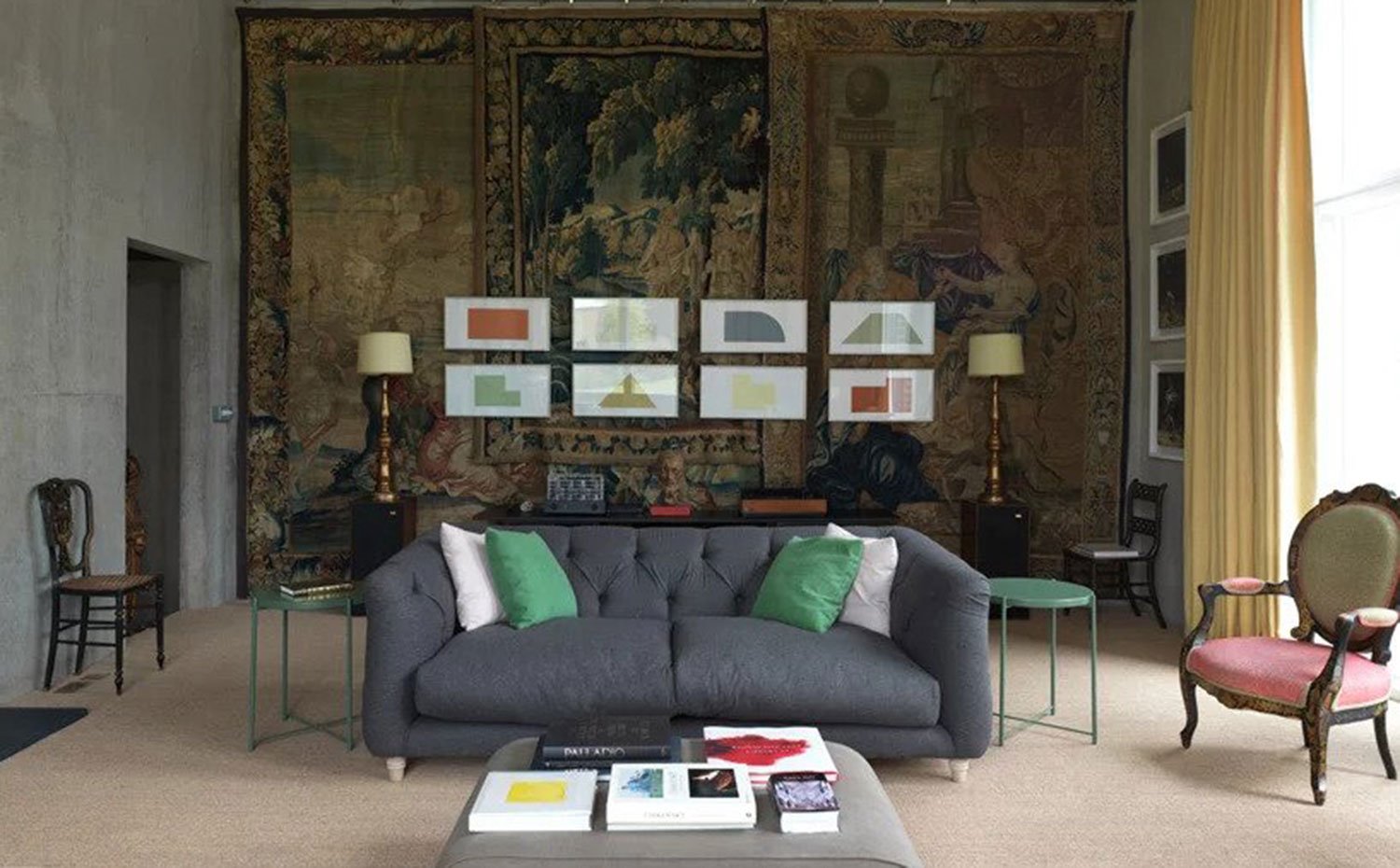 Sofá gris en centro de salón, mesillas auxiliares en verde, butacas y sillas clásicas, tapices en la pared superpuestos