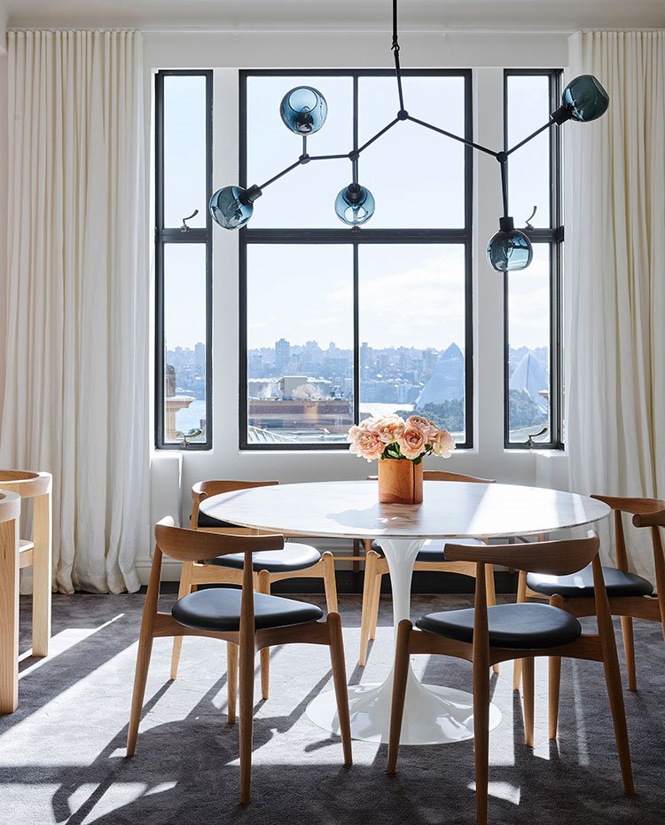 Comedor con mesa circular blanca y sillas de madera con asiento de piel negro, luminaria suspendida con esferas de cristal azul