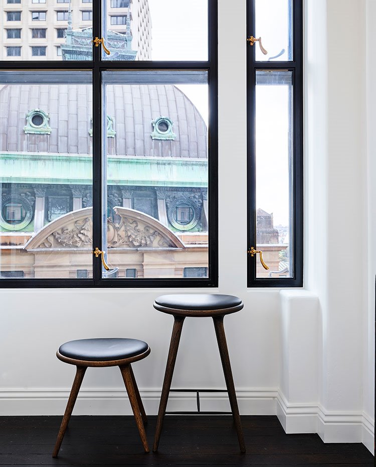 Detalle taburetes en diferentes alturas en madera y piel, ventanas con cerramiento vintage de doble cristal.