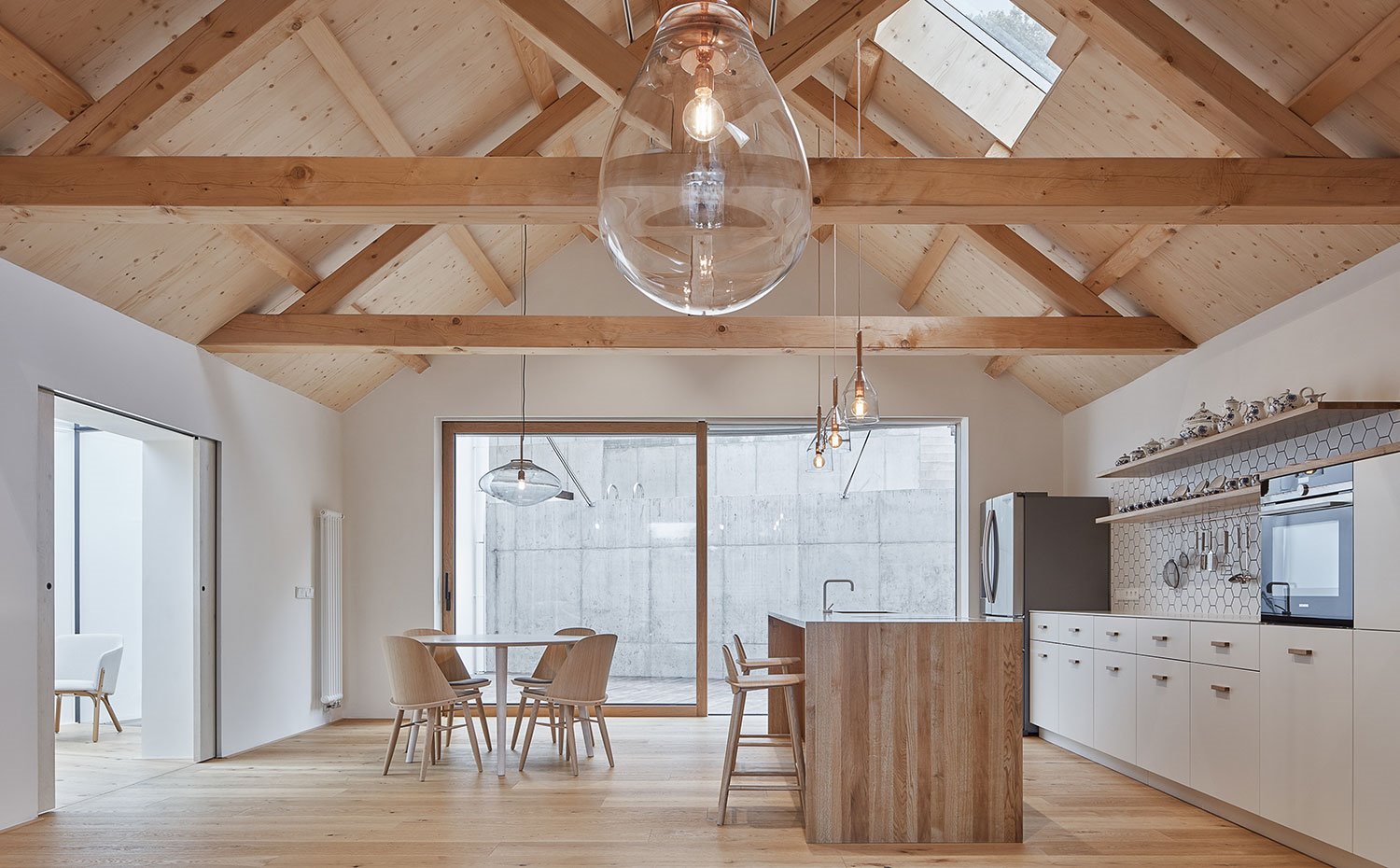 Cocina abierta con isla de madera, techo a dos aguas, mesa de comedor con sillas de madera