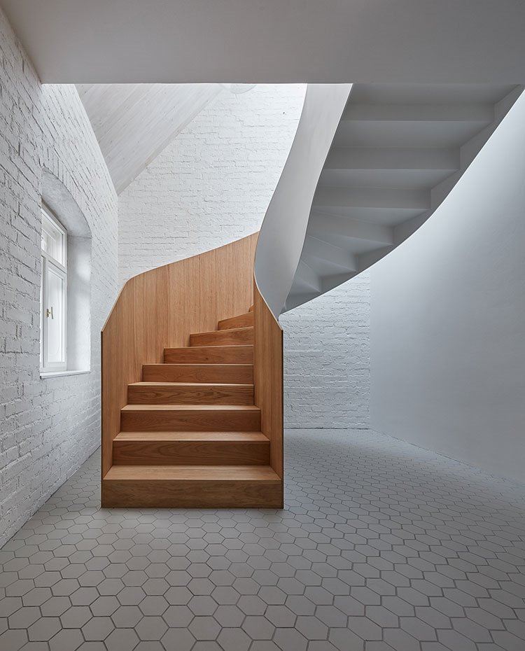 Escalera de caracol revestida de madera en su parte interior, baldosas de suelo hexagonales, pared de ladrillo visto