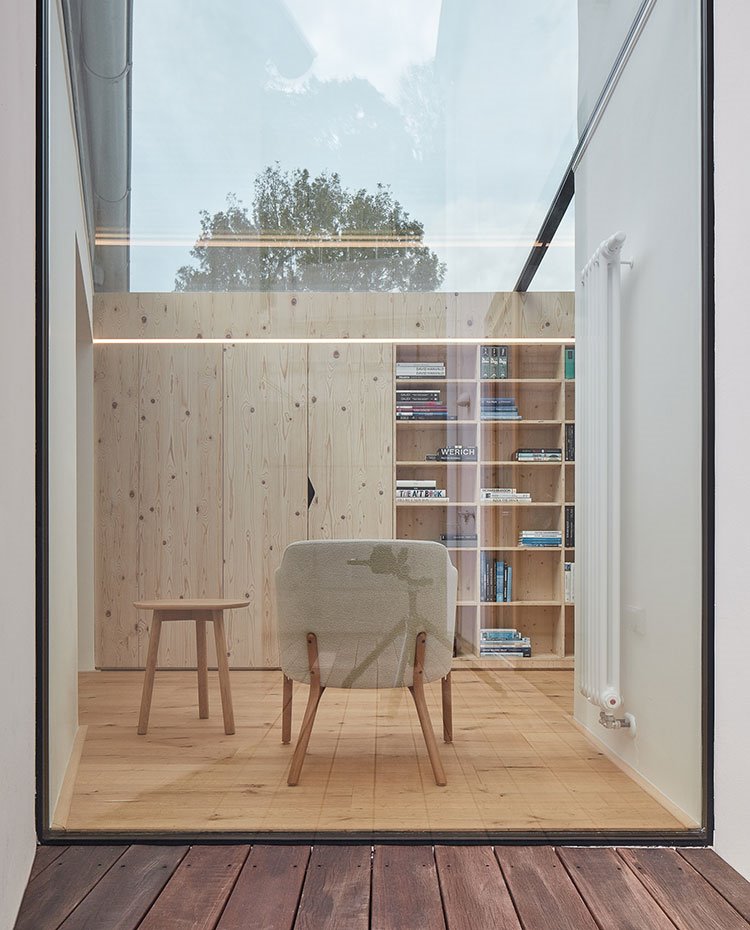 Tarima exterior de madera, tabique de cristal hacia interior con butaca, silla y armarios y estantería a medida.