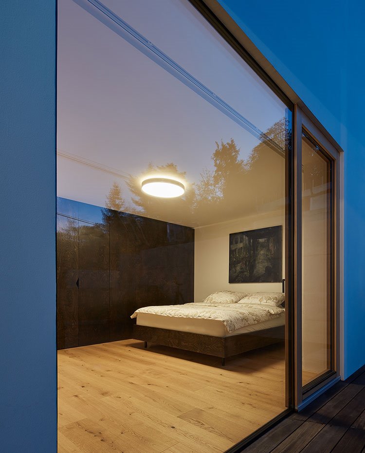 Vista de dormitorio desde exterior con cerramiento acristalado, suelo de madera, armario de madera, plafón en techo