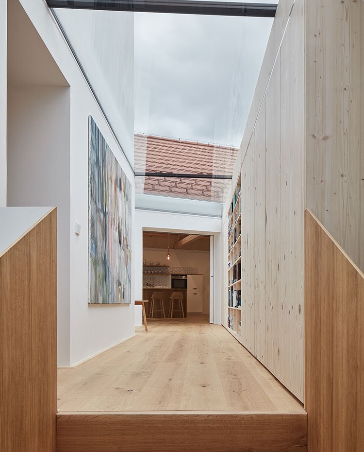 Zona de paso con suelo de madera, techo de cristal, armarios y estantería empotrada a pared