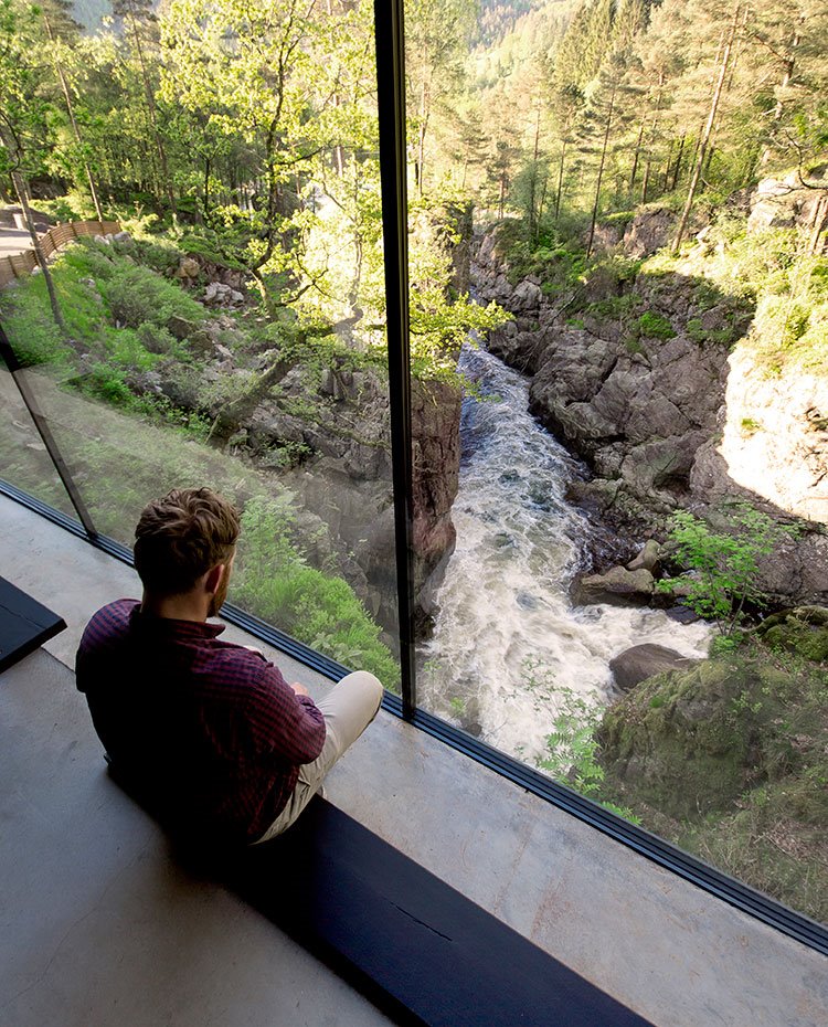 Asientos adaptados al extremo del interior de la casa para observar el salto de agua en medio de la naturaleza