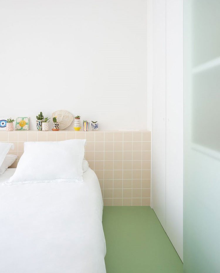 Dormitorio con lencería de hogar en blanco, suelo verde y murete revestido de baldosas en color crudo