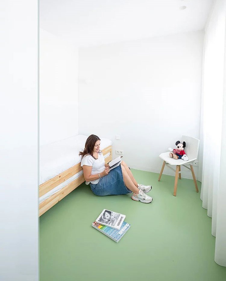 Dormitorio infantil con cama de madera, silla en blanco y madera y suelo en verde