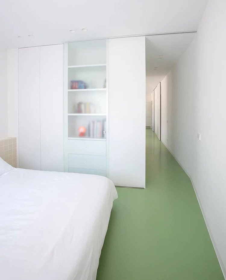 Dormitorio principal con armario de obra en blanco y cristal traslúcido, suelo en verde y pasillo hacia salón