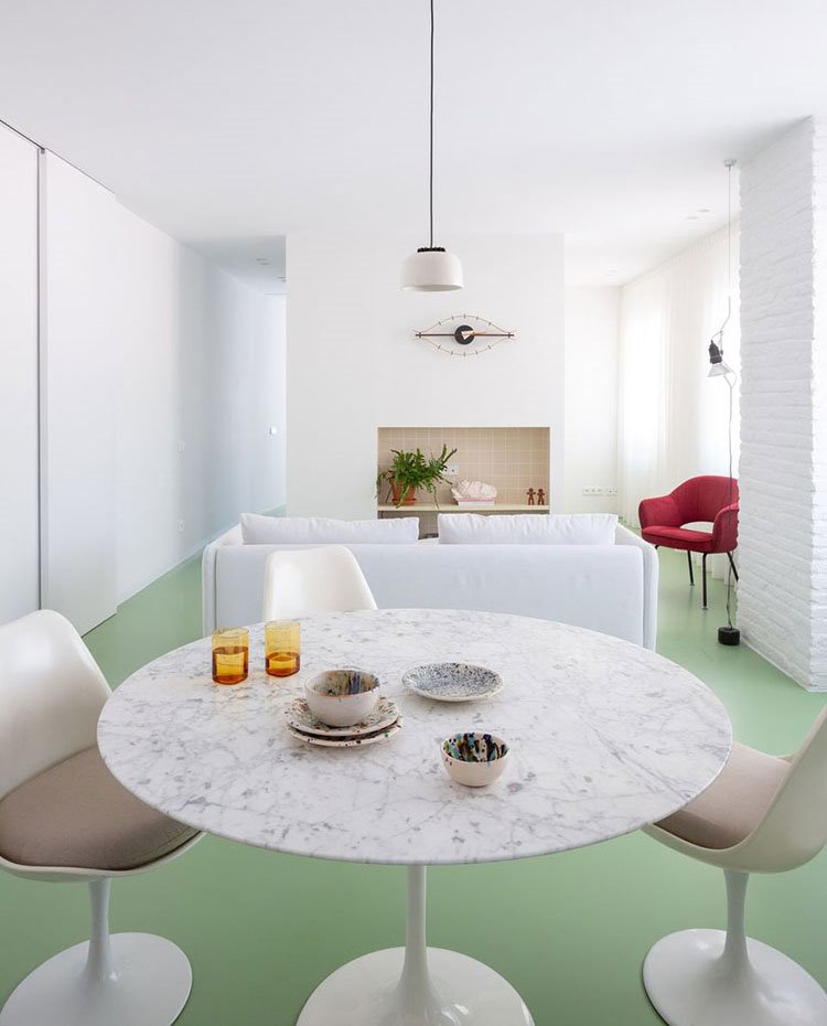 Mesa redonda con sobre de mármol, sillas blancas con asiendo en beige, sofá blanco y butaca roja