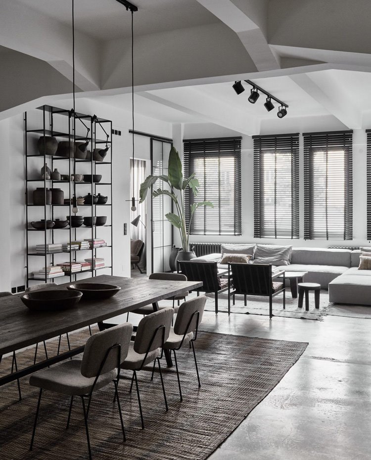 Comedor con luminarias suspendidas sobre la mesa de madera y focos alineados en la zona de salón, con grandes aperturas hacia el exterior