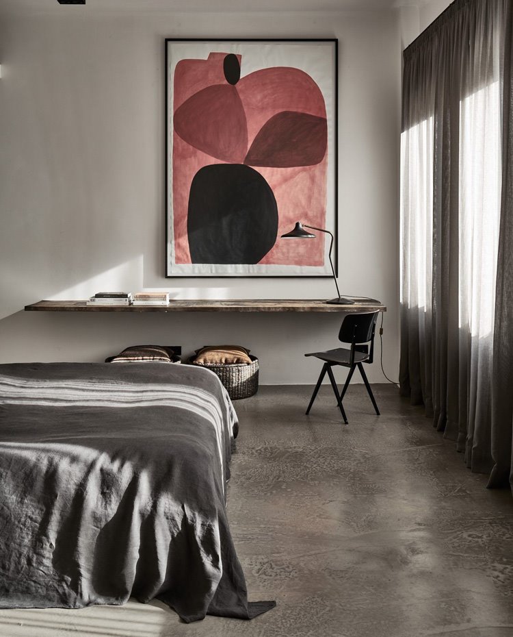 Dormitorio con ropa de cama en gris, y zona de trabajo con balda sujetada en pared y silla, todo de madera.