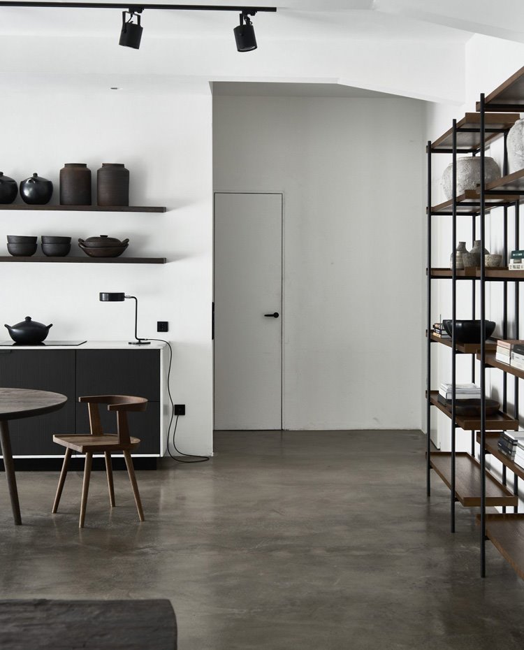 Estantería de madera y acero en negro, suelo de hormgión, mesa y silla en madera y módulo contenedor con estructura en blanco y frentes en madera de wengué