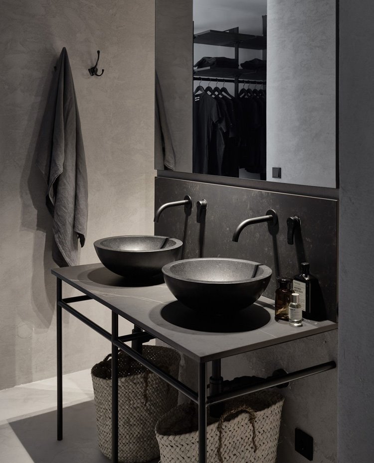 Lavamanos de cuarto de baño con estructura de piedra y hierro, lavamanos circulares y grifería en negro, cestos en la parte inferior