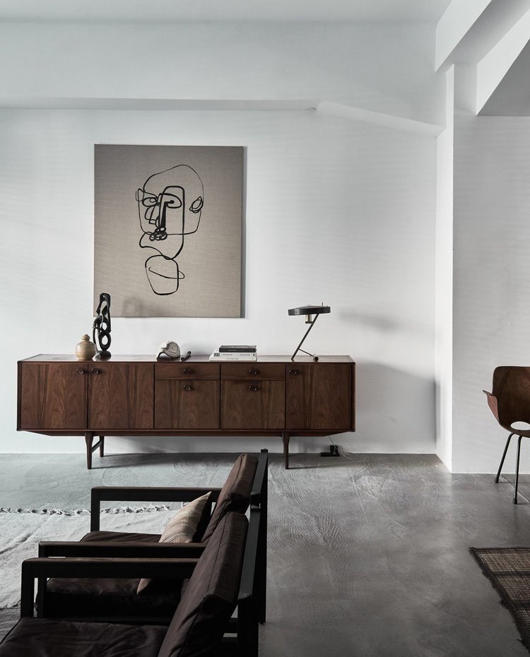 Mueble contenedor en salón, de madera oscura, junto a butacas de madera y tapicería en marrón oscuro.