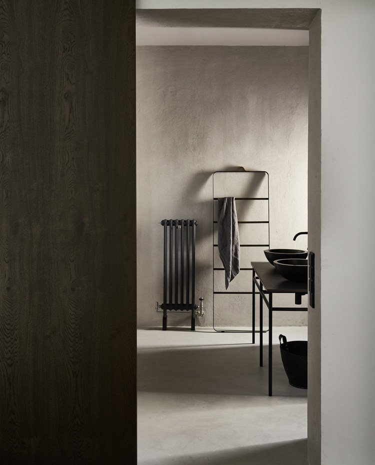 Puerta corredera hacia cuarto de baño, revestido de hormigón, con radiador en pared gris oscuro, toallero y zona de lavamanos