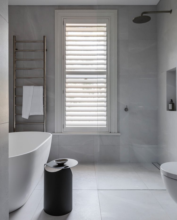 Cuarto de baño revestido de mármol, mampara de cristal transparente, bañera exenta, toallero de pared cromado