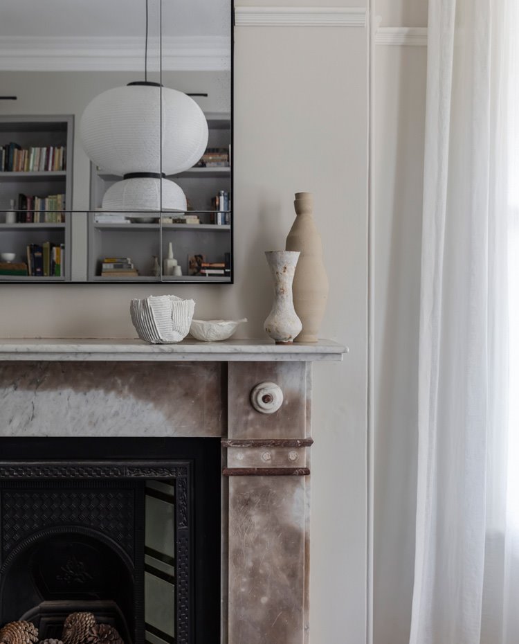 Detalle chimenea revestida de mármol, espejo superior, cortinas en blanco frente a ventanales