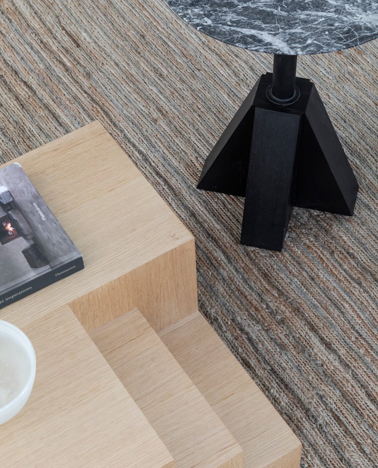 Detalle mesa de centro en madera clara, alfombra de rica textura y mesilla auxiliar con sobre en mármol redondo