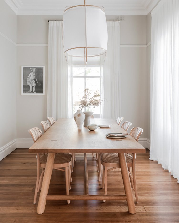 Mesa y sillas de comedor de madera, en acabado natural, luminaria suspendida en blanco y madera, suelo de madera y grandes aperturas con cortinas en blanco