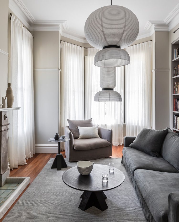 Salón con alfombra y sofá en gris, sillón en tonos tierra y grandes ventanales con cortinas