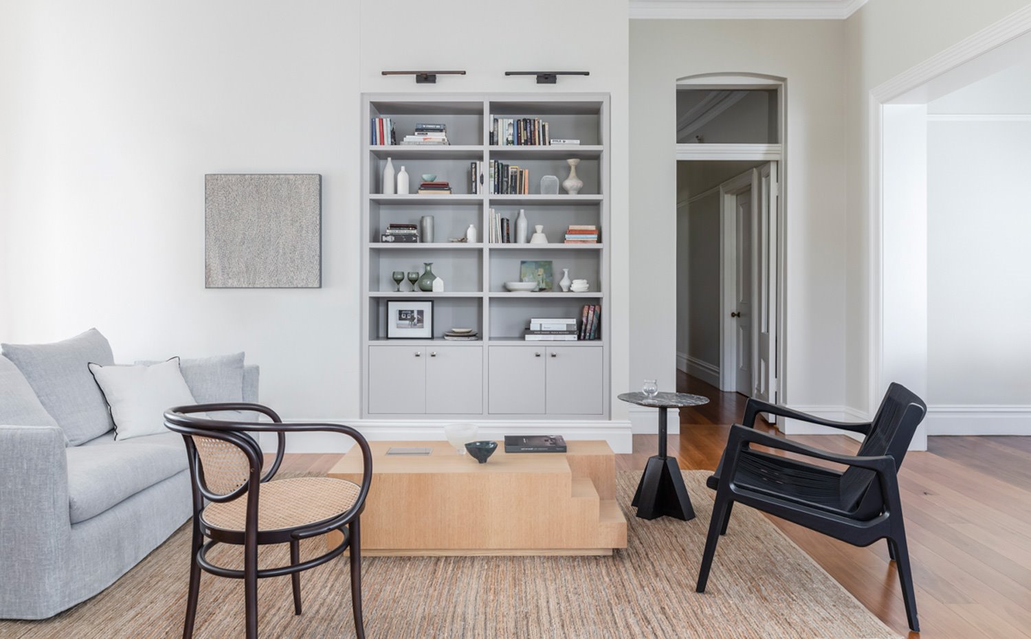 Zona de estar con sofá gris claro, butacas vintage, mesa de centro de madera, alfombra en marrón sobre suelo de pared