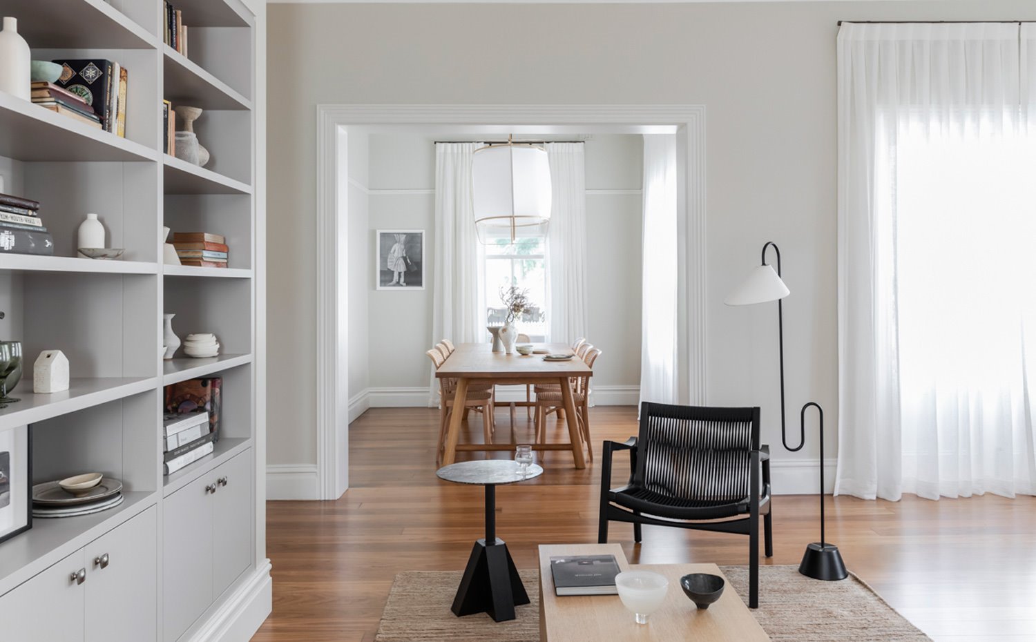 Zona de estar junto a comedor con butaca en tonos marrón oscuro, librería integrada en frente de pared y mesa de centro de líneas geométricas