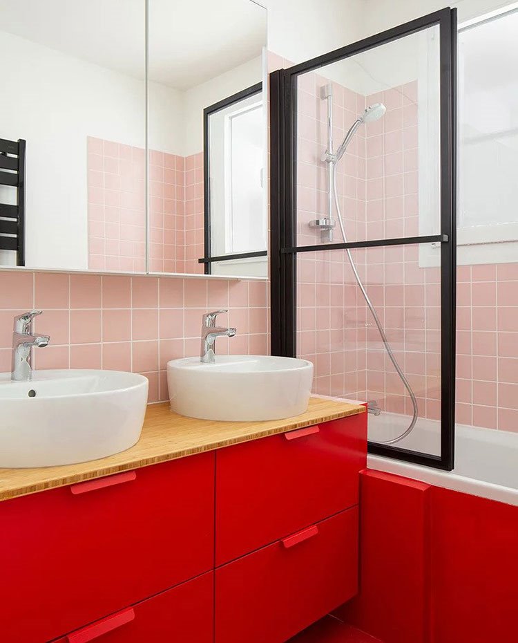 Cuarto de baño con armarios bajo lavamanos en rojo, revestimiento en rosa, mampara con perfilería en negro