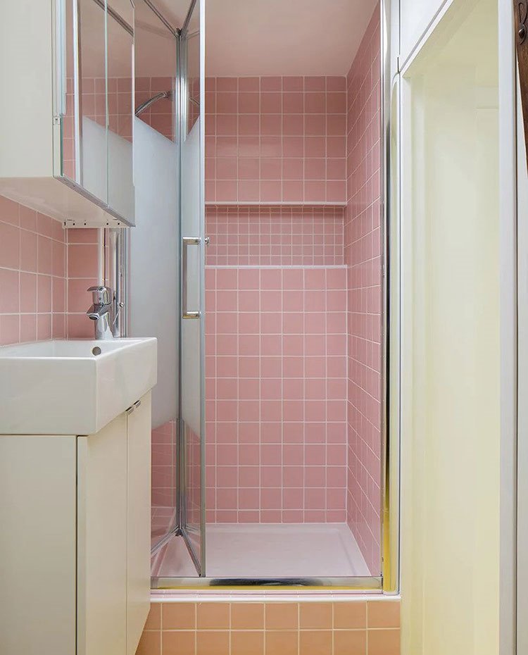 Cuarto de baño con mobiliario en blanco, mampara con perfilería cromada brillante y cristal translúcido y revestimiento en rosa