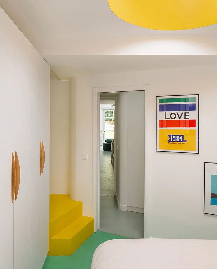 Dormitorio con escaleras en amarillo, suelo en verde y resto de estancia en blanco