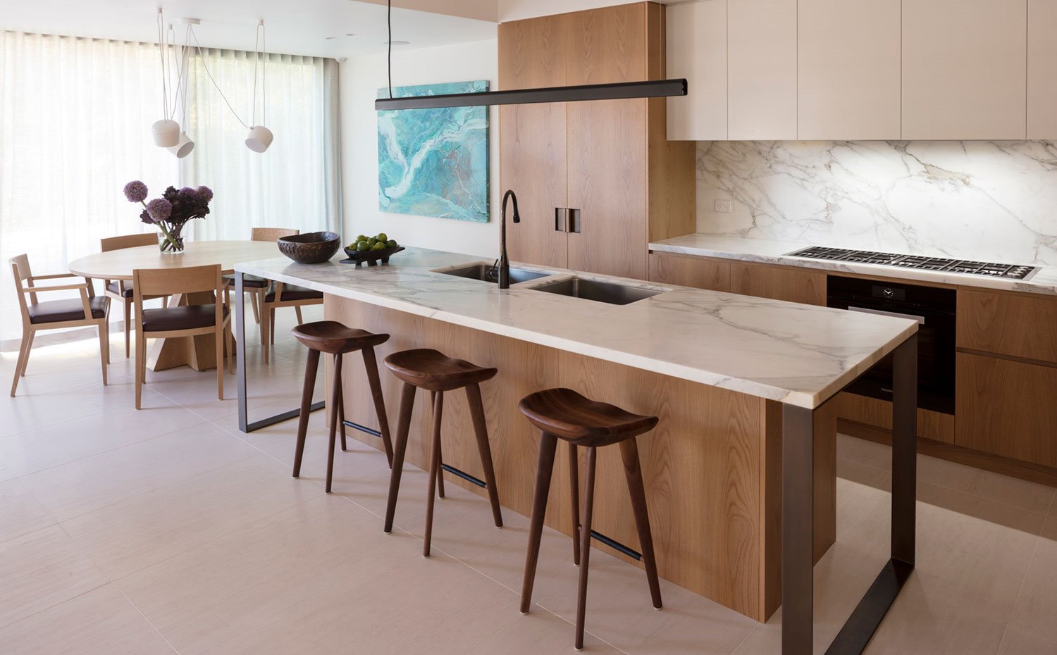 Isla de trabaja con encimera de mármol, taburetes de madera y al fondo mesa y sillas de comedor
