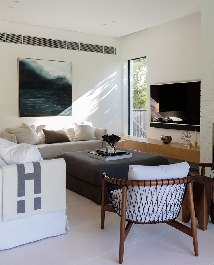 Salón con sofás en crido, butacas en madera y pouf central en gris oscuro