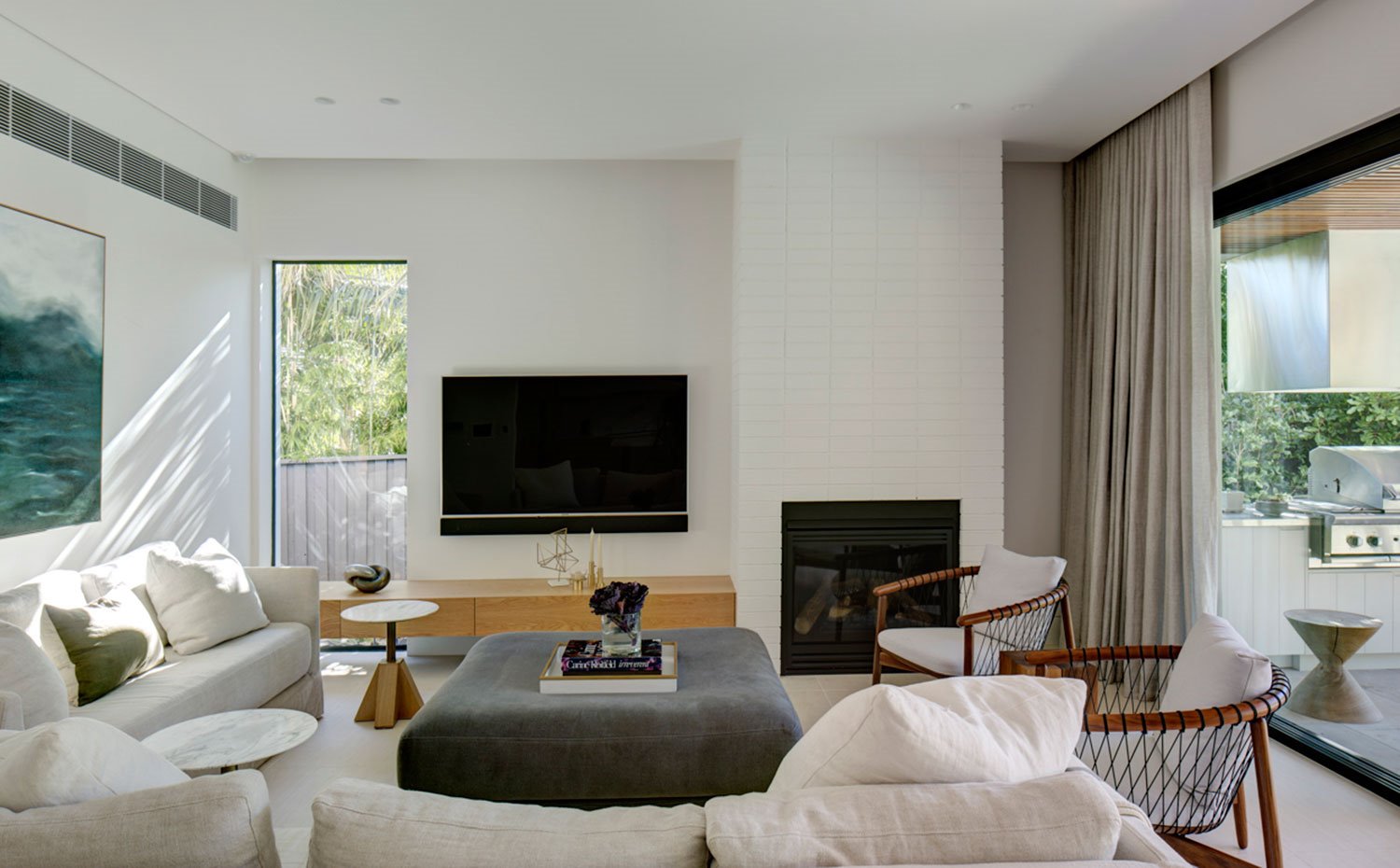 Salón con sofás en crudo, pouf central en gris y butacas en madera y cojines blancos