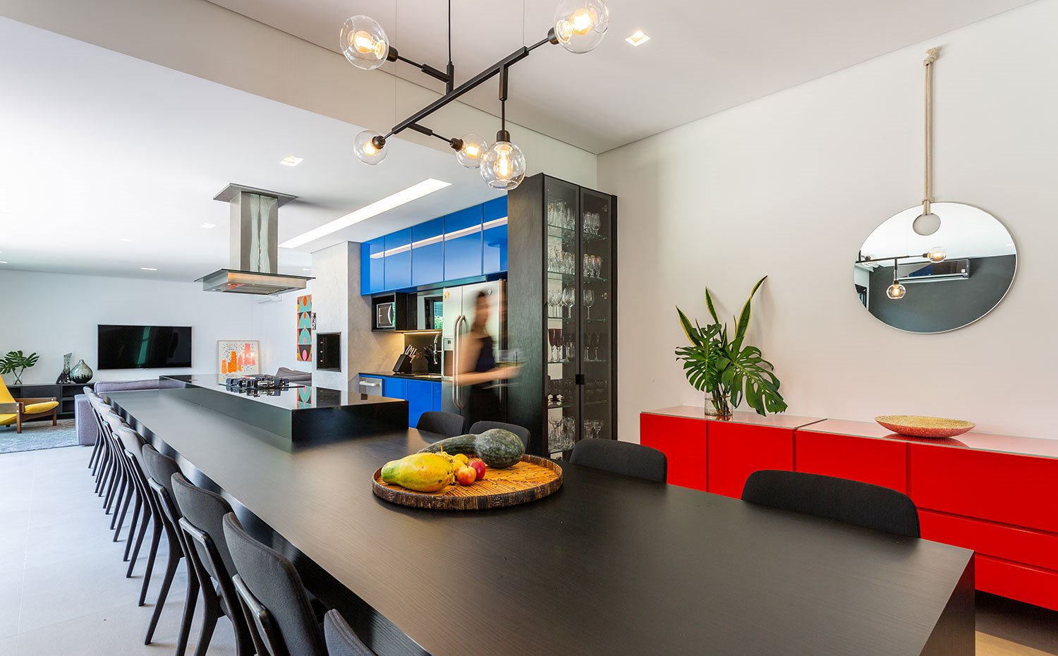 Cocina con isla y gran mesa con numerosas sillas a juego en nogro, mueble contenedor en rojo 